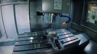 Рабочая зона SMTCL VMC850Q в работе: шпиндель с фрезой над заготовкой в тисках, стол с Т-пазами